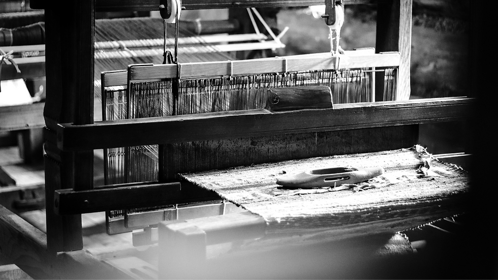 Black-and-white image of a vintage weaving loom with threads and wooden parts. The setting is rustic, creating a nostalgic and tranquil mood.