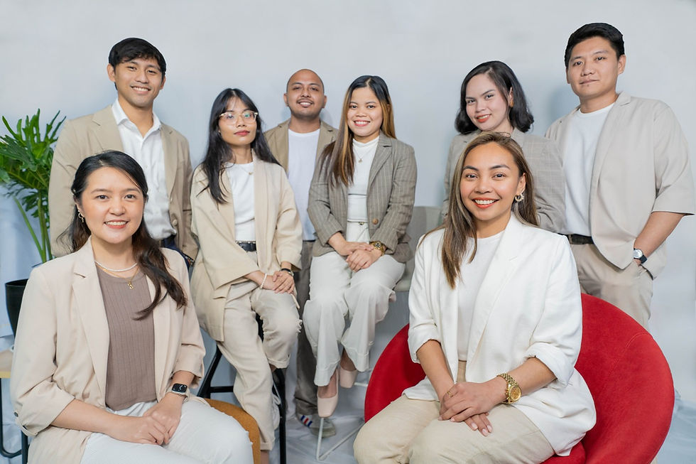 OFFICIAL STUDIO-ID8 TEAM PHOTO, wearing beige suits, in a bright room with a green plant. One sits on a red chair, conveying a cheerful mood.
