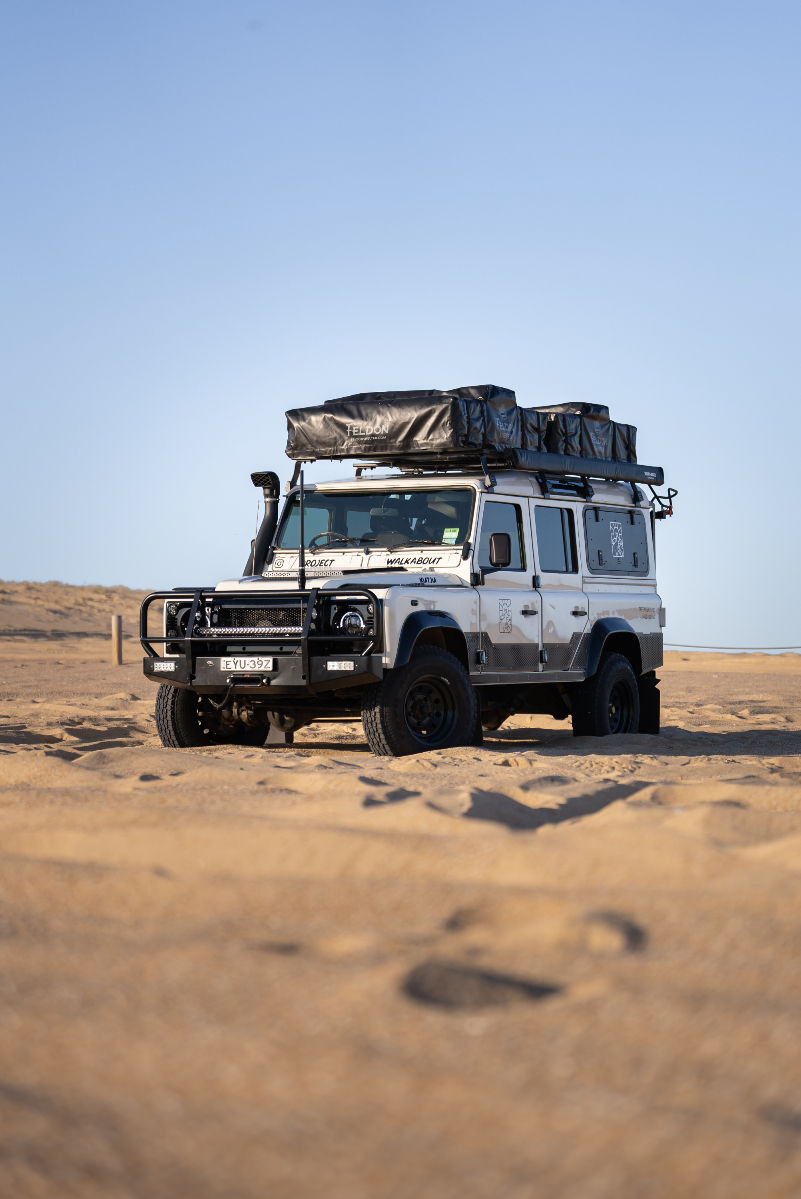 High angle view of a Land Rover Defender overlander crossing a shallow river in a forest