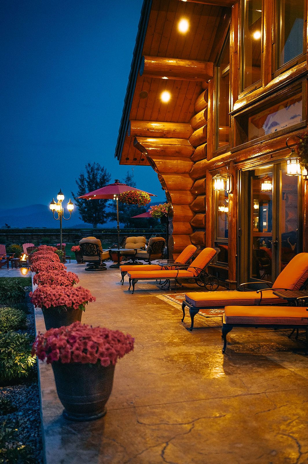 Lounge chairs and potted flowers on the lit patio at dusk