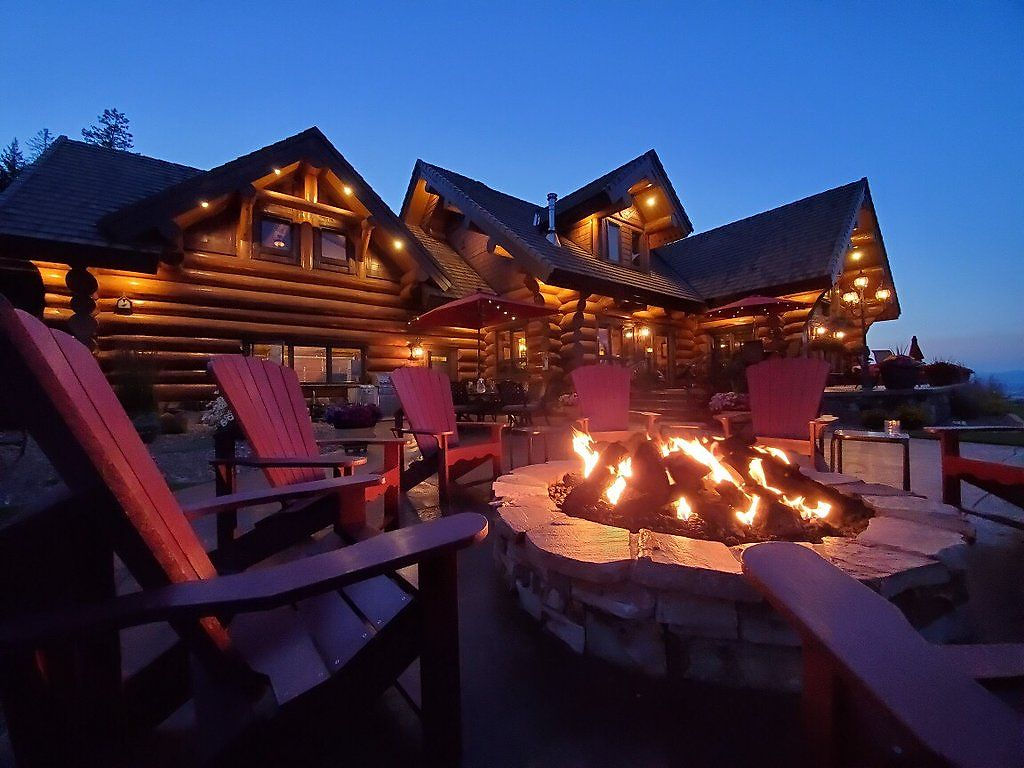 Red chairs around the glowing fire pit on the stone patio at dusk