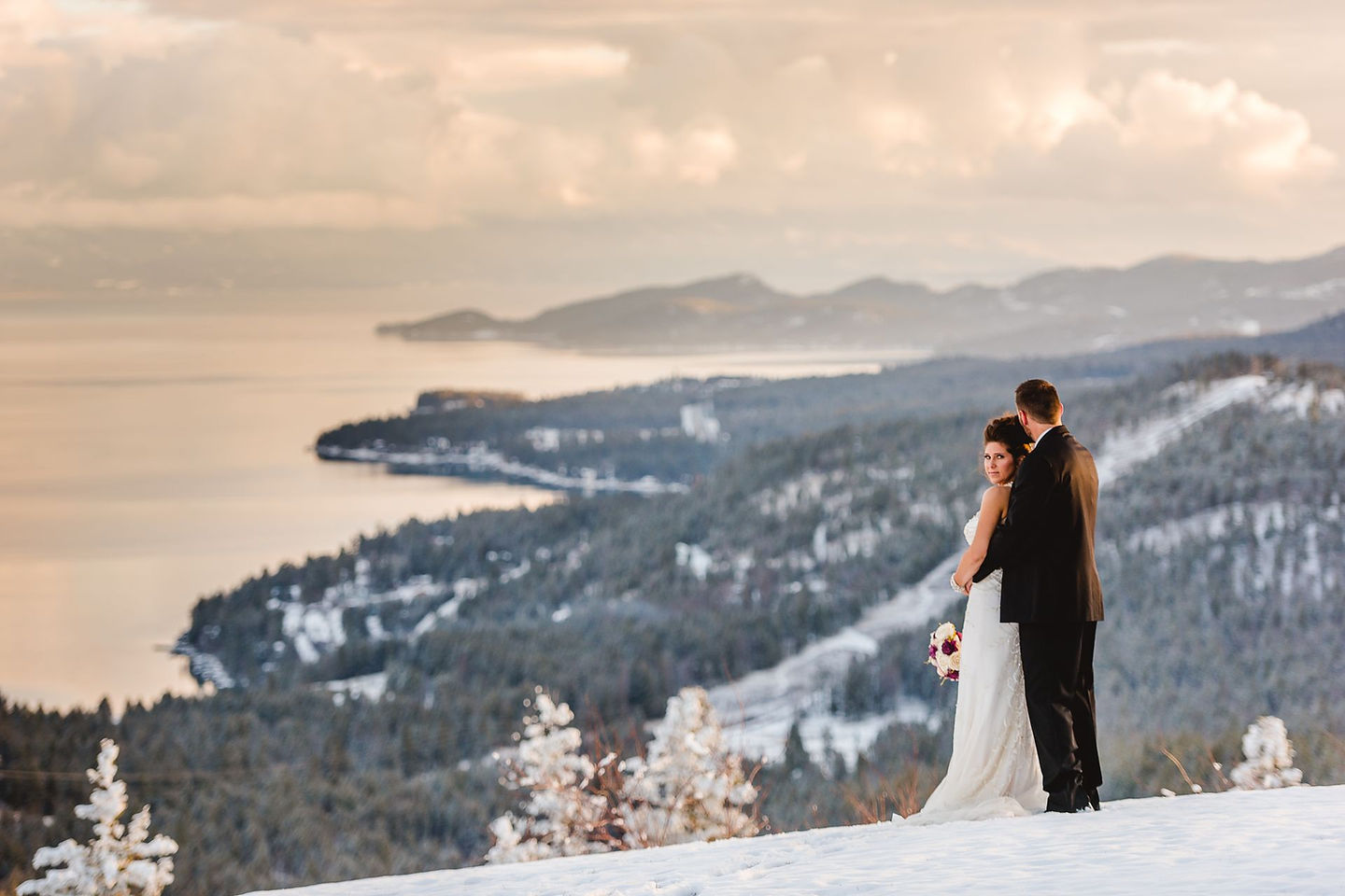 A bride and groom in the snow on the bluff, Flathead Lake far below