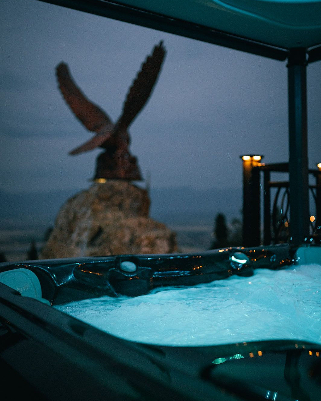 A private hot tub glowing at dusk beside a carved eagle sculpture