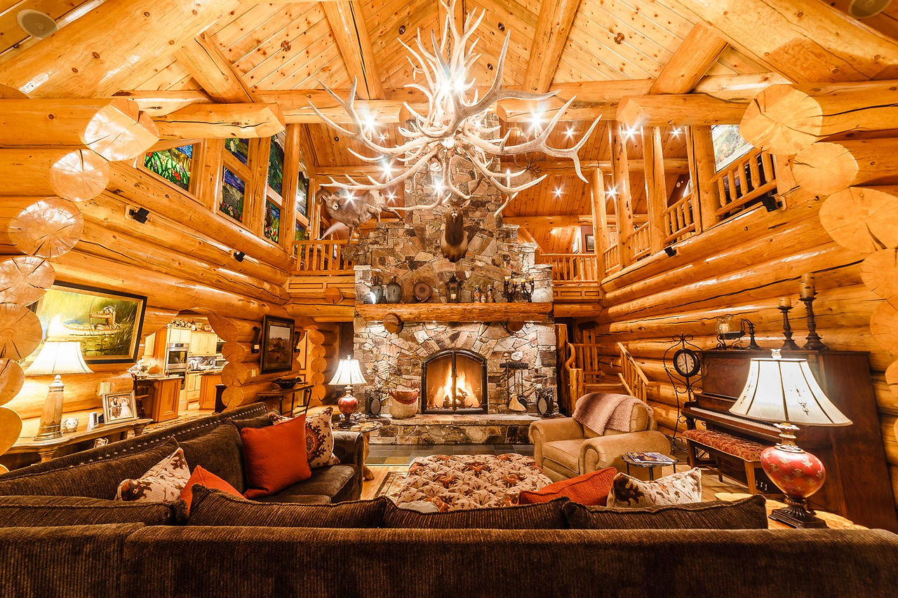 Great room with a stone fireplace, antler chandelier and log walls