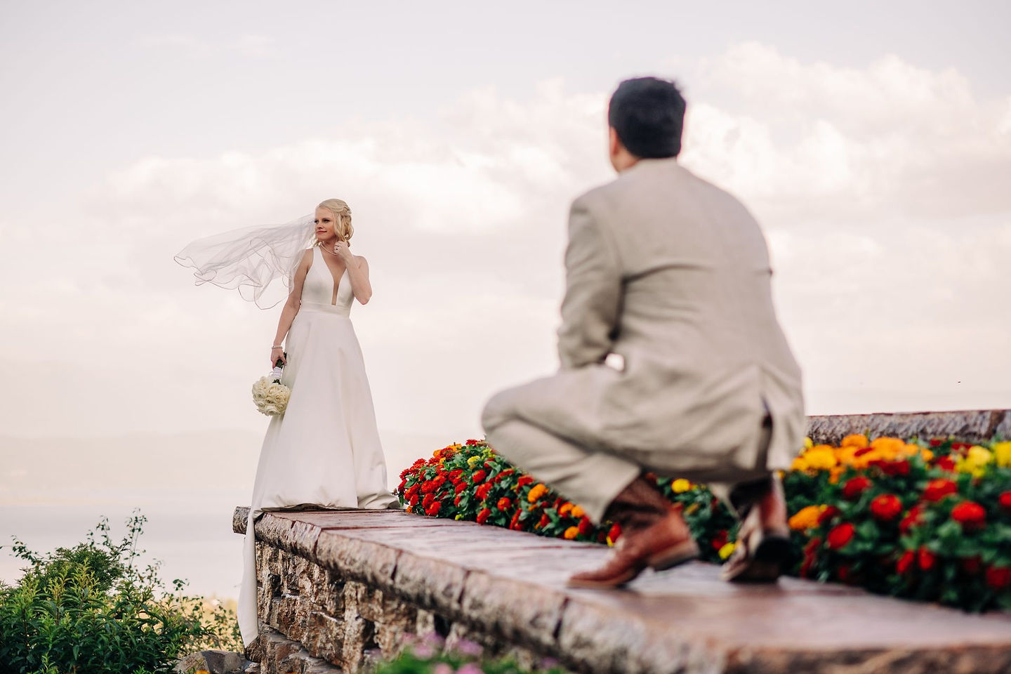 A bride and groom on the stone wall above the valley, flowers at their feet