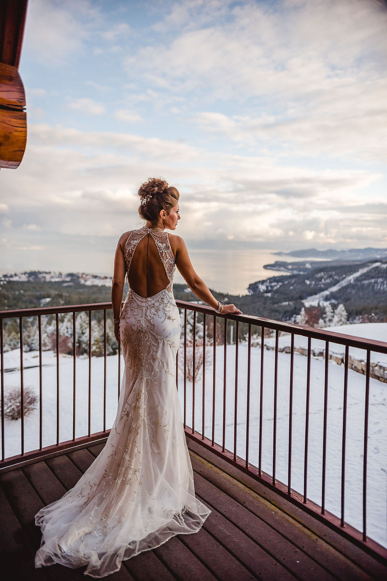 A bride on a snowy balcony overlooking the lake and mountains