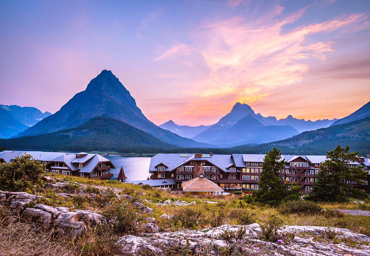 Alpine lodge and lake beneath snow-capped peaks at sunset