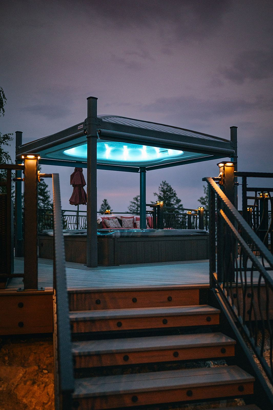 Lit deck stairs leading up to the hot-tub gazebo at dusk