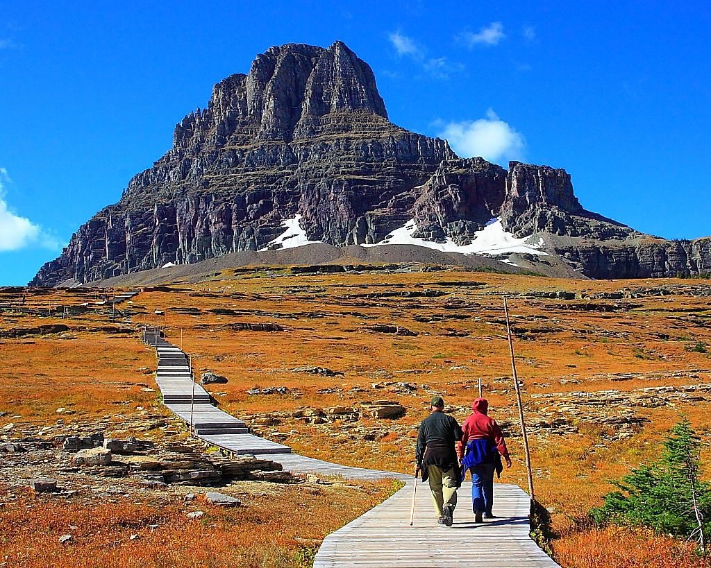 Hikers on the boardwalk toward a towering rock peak