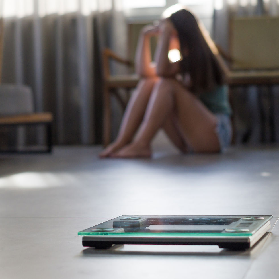 Bathroom scale in the foreground with a blurred person sitting on the floor in the background, appearing distressed