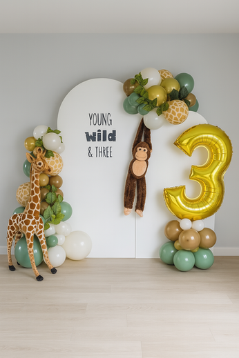 Safari-themed third birthday party decor with a large gold number '3' balloon, a cute giraffe prop, and a modern arched backdrop reading 'Young, Wild & Three'.
