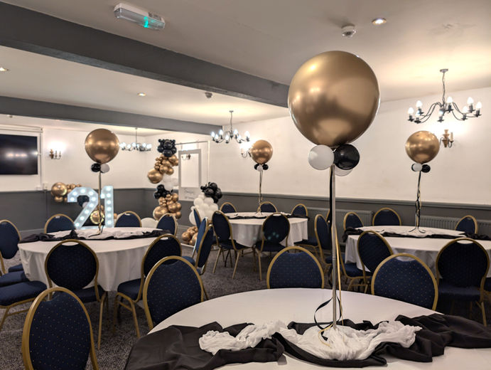 Modern 21st birthday party setup with black and white tables, gold orb balloon centerpieces, and a "21" light-up number