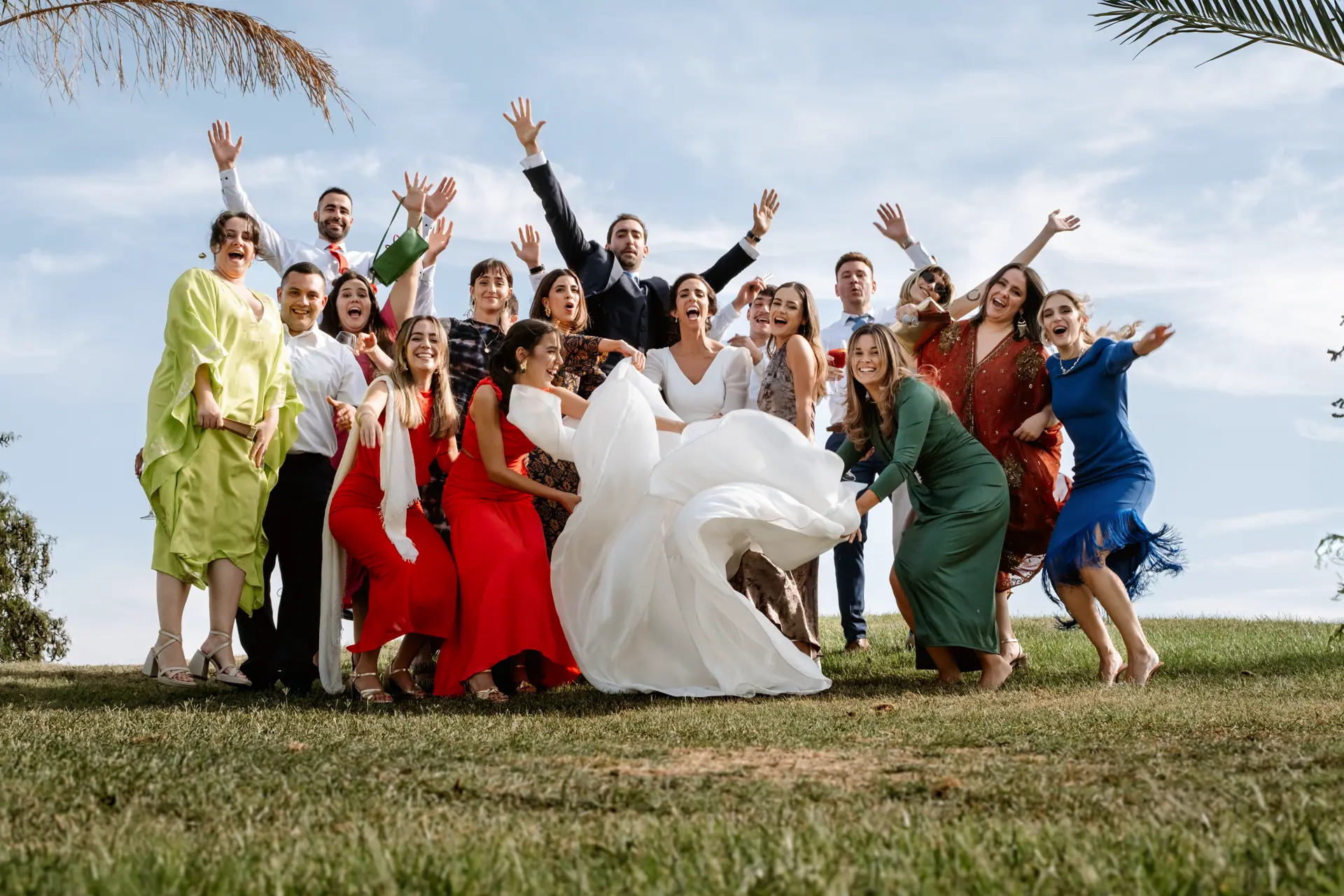 Una radiante novia y su recién estrenado esposo, rodeados de familiares y amigos, comparten un momento de alegría y celebración en el campo de golf Guadiana en Badajoz. Los invitados, ataviados con elegantes vestidos y trajes, levantan las manos al aire en un gesto de felicidad y unión, mientras la pareja de novios se destaca en el centro, capturando la esencia de un día memorable.