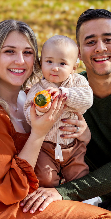 Happy family portrait: parents and baby with pumpkin