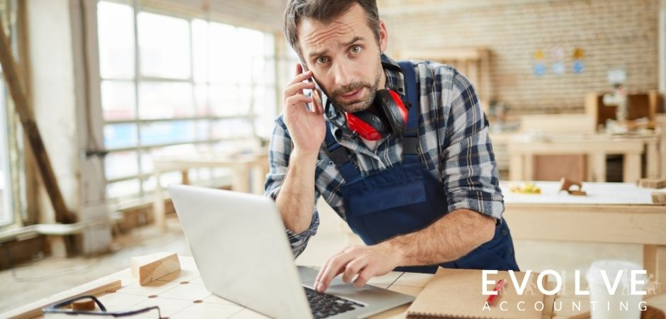 Man in woodwork workshop standing at laptop on cellphone
