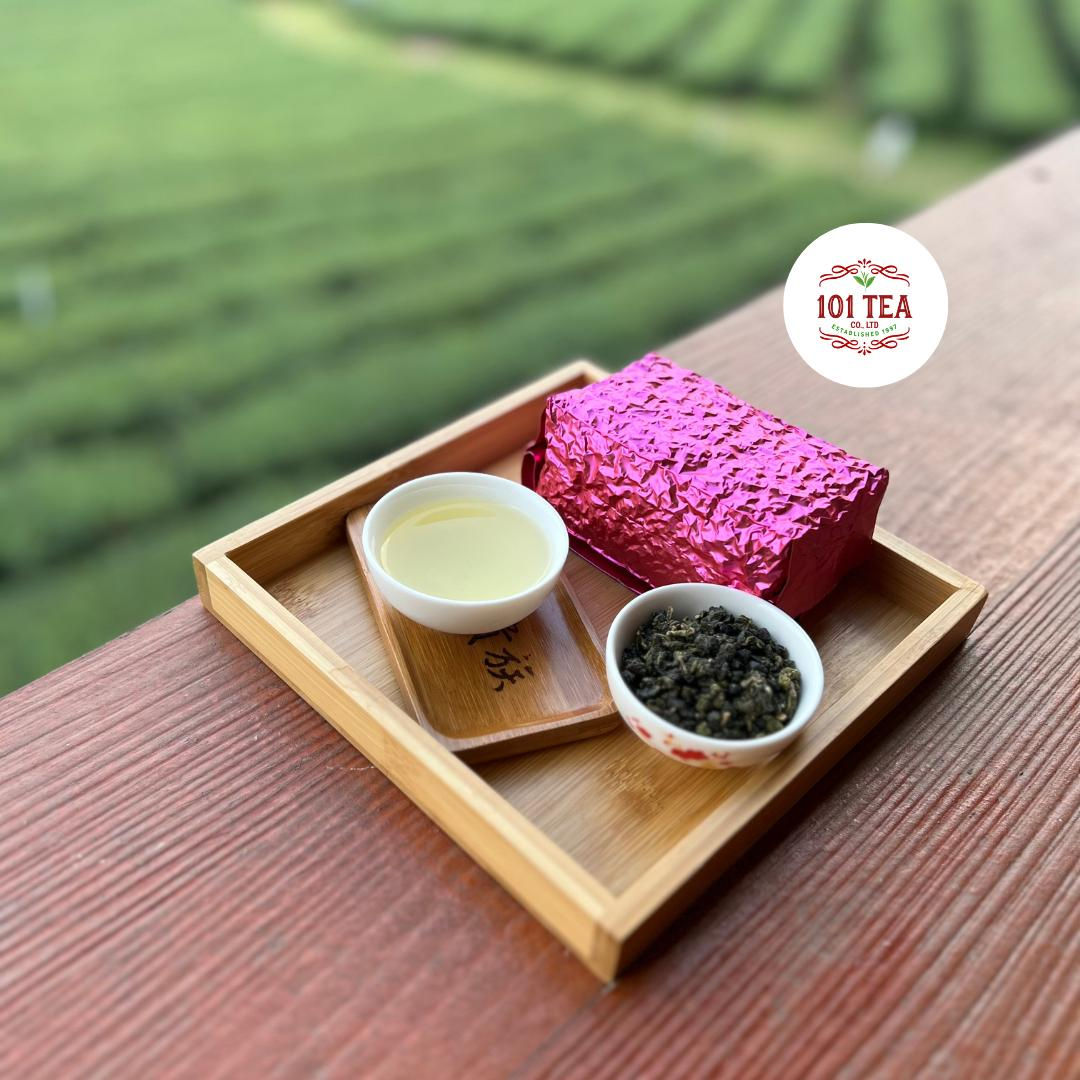 Four Seasons Oolong with brewed tea, loose leaves, and a pink package on a wooden tray.