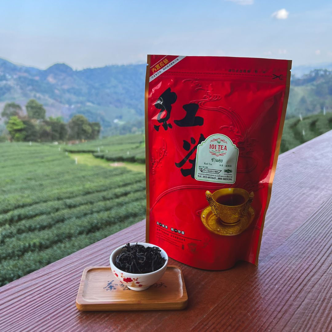 101 Tea Red Oolong bag with gold teacup design, a small bowl of loose leaves on a wooden ledge, tea fields and hills behind.
