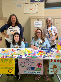 Three women and a girl pose behind a table displaying homemade crafts and signs encouraging people to purchase the items to support the Bert Nash Center