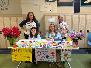 Three women and a girl pose behind a table displaying homemade crafts and signs encouraging people to purchase the items to support the Bert Nash Center