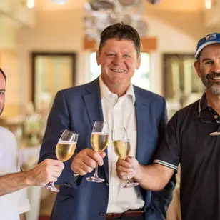 Three men toasting with champagne glasses indoors at a winery