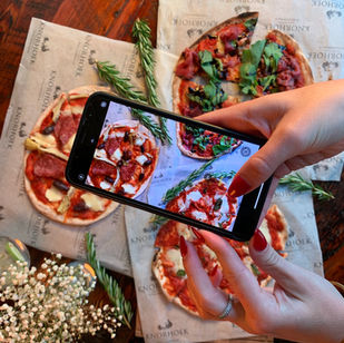 hand holding phone above pizzas