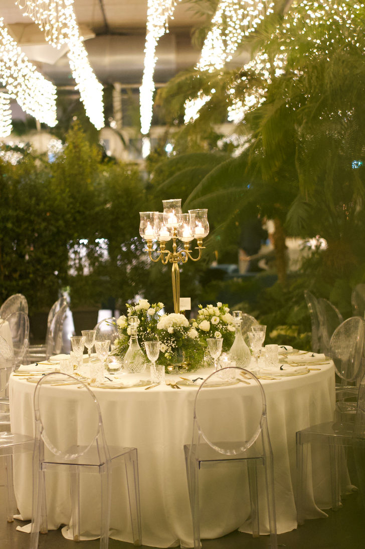 Tavoli del ristorante con luci soffuse decorati con centrotavola floreale e candelabro dorato, candele accese e luci cadenti dal soffitto per atmosfera romantica