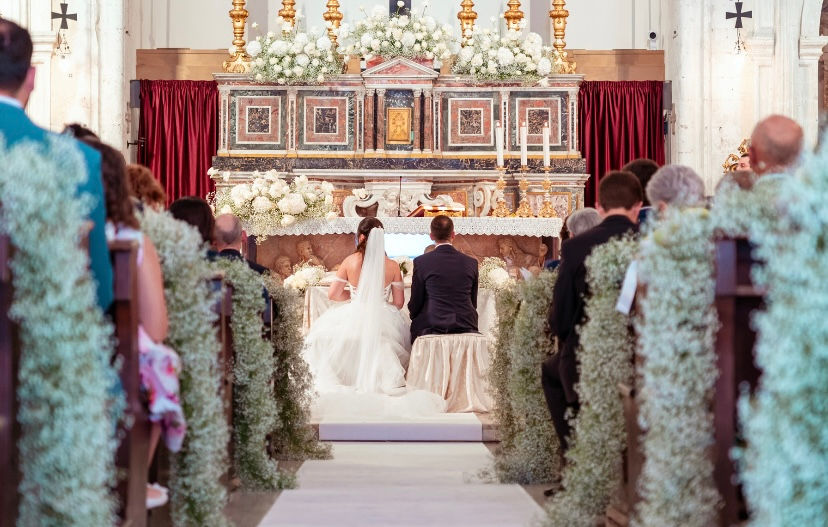 Primo piano della navata centrale del duomo di Taormina addobbato con fiori e sposi di fronte al sacerdote