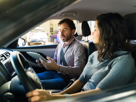 Young woman taking her driving exam and learning to drive vehicle assisted by her teacher, sitting inside modern car