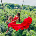 Chelsea Alberti wearing a beautiful dress while swinging with a scenic Bali landscape behind her.