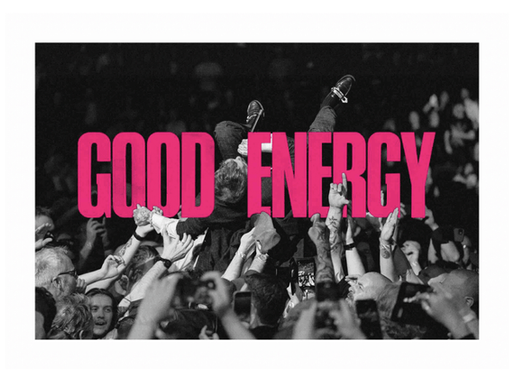 Crowd surfer supported by fans in black-and-white photo with bold pink text "GOOD ENERGY" overlay. Energetic concert vibe.