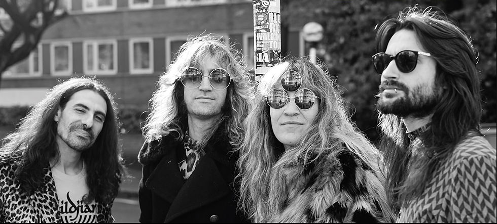 Four long-haired men in sunglasses pose outdoors in black and white, one wearing a leopard-print jacket and a visible band T-shirt.