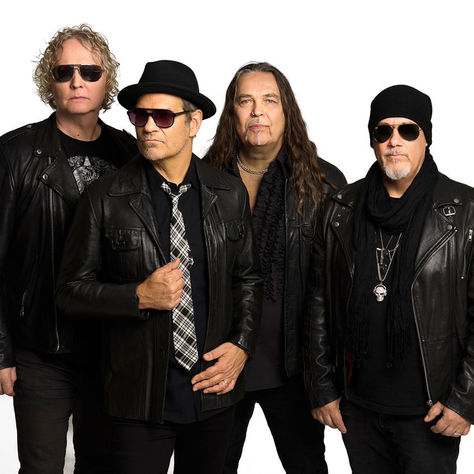 Four men in black leather jackets and sunglasses pose against a white studio background, looking serious and cool.