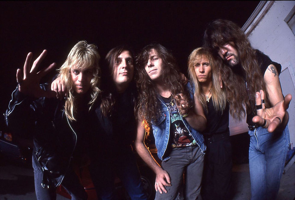 Five long-haired rock musicians pose closely in a dark backstage setting, one reaching toward the camera.