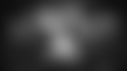 Six men in dark suits with skull pins pose against a moody backdrop. One in front gestures with fingers. Black and white photo.