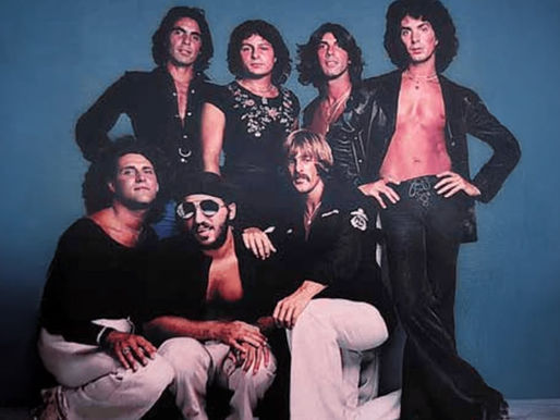 Seven people pose confidently against a blue background, wearing black and white clothing. The mood is retro and stylish.
