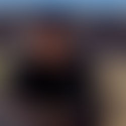 Man in a black hat and sweater gazes to the side, seated in a sunny desert landscape with rocky hills, creating a contemplative mood.