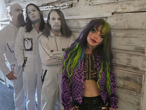 Three people in white costumes with white face paint and a woman in a purple checkered jacket with green hair against a rustic wall.