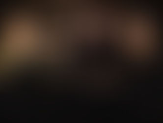 Four men with long hair and serious expressions stand against a wooden background. One wears a camouflage cap, another has crossed arms with tattoos.