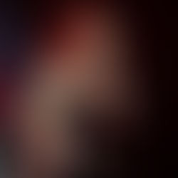 Rocker with curly hair and tattoos sings passionately into mic on stage. She's wearing a black outfit with floral patterns. Dark background.