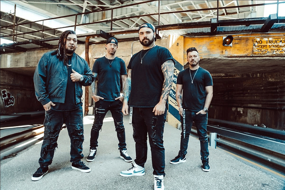 Four men stand confidently in an urban setting, wearing black outfits and sneakers. A "NO TRUCKS" sign is visible in the background.