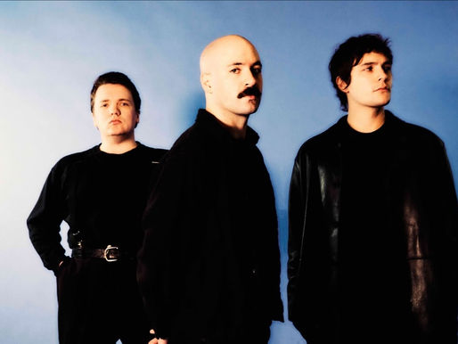 Three men in black clothing stand against a blue background, looking serious and composed. The mood is formal and focused.