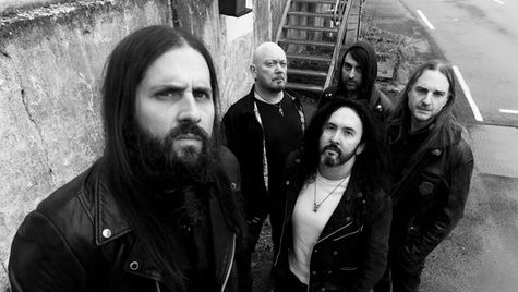 Five men in leather jackets stand on a street, looking up seriously. There's a concrete wall and metal stairs in the background. Monochrome.