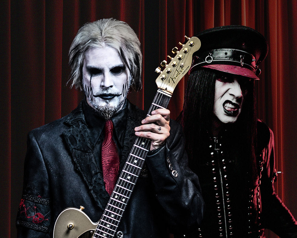 Gothic musician with white face paint holds a Fender guitar before red curtains, beside another dark-clad performer in a fierce pose