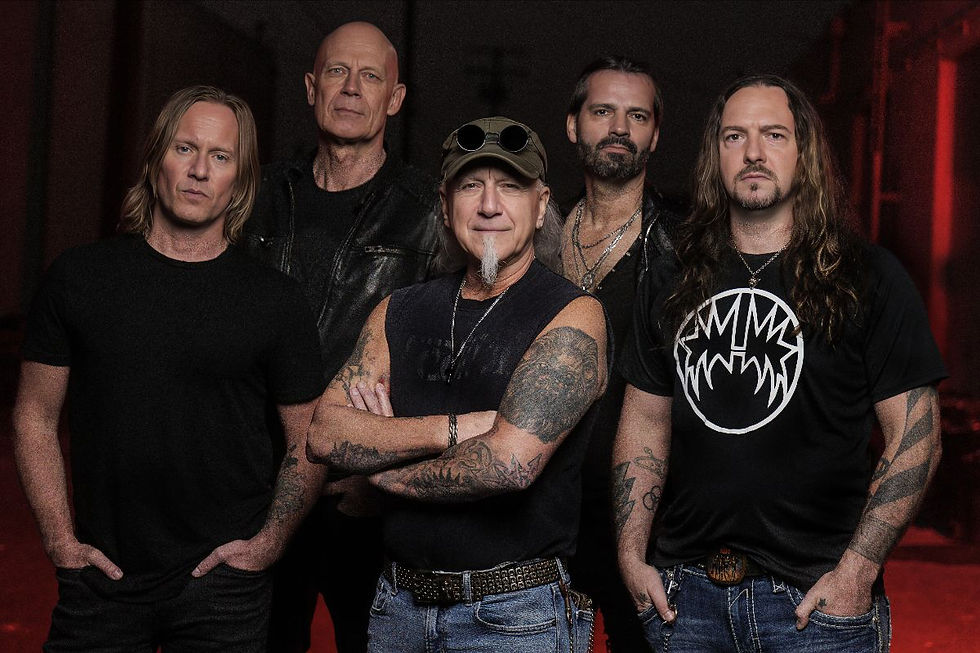 Five rock musicians pose in black shirts against a dark red backdrop, arms crossed and serious, with tattoos and a band logo tee.
