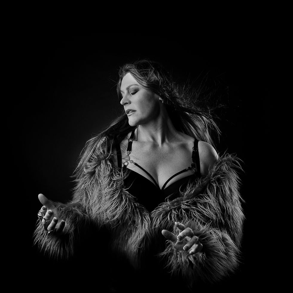 Black-and-white portrait of a woman in a fur coat and lingerie, eyes closed, hands outstretched against a dark background.