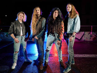 Four men with long hair stand confidently on a graffiti-covered street at night, lit by blue and red lights, wearing leather and denim.