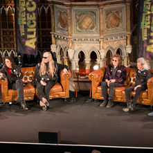Five people sit on stage in a panel discussion, with "The Reverend Alice Cooper" banner behind them. Ornate backdrop and casual setting.