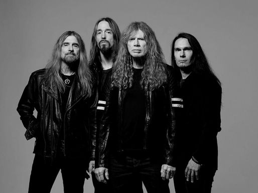 Four men with long hair in black leather jackets stand against a gray background, displaying a serious demeanor.