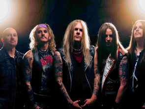 Five men with long hair and tattoos in rocker attire pose under bright lights, exuding a bold and edgy vibe.