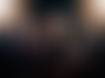 Five tattooed rock musicians with long hair and leather vests pose under bright lights. Intense expressions. Dark background.